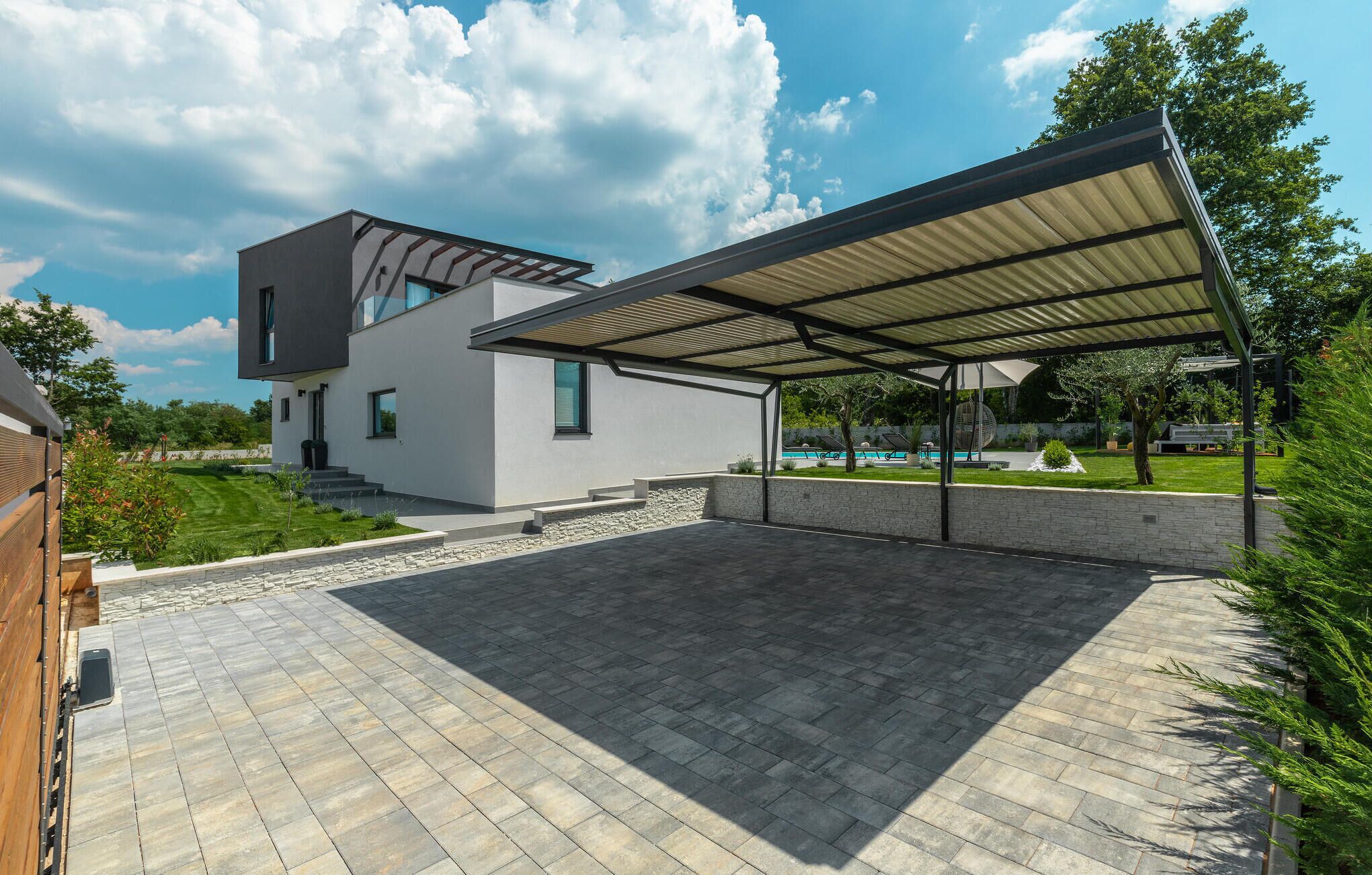 Ein modernes Haus mit überdachter Terrasse, Swimmingpool und gepflegtem Rasen.