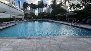 A swimming pool with lounge chairs and umbrellas, surrounded by palm trees and high-rise buildings. - Golden Bay 608, (Sunny Isles Beach)