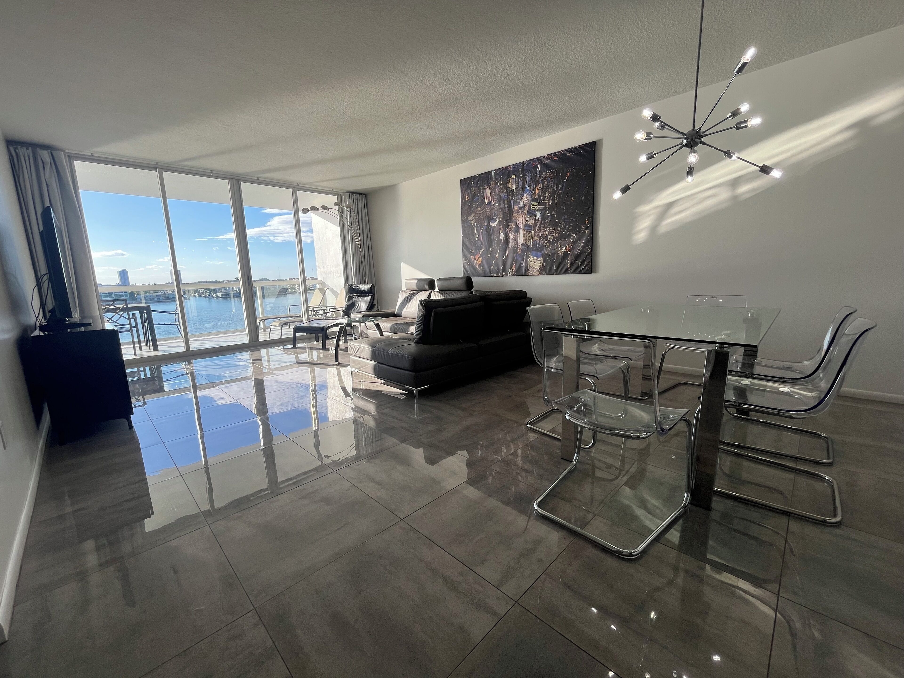 A modern living room with a glass dining table, leather sofa, and a large window overlooking a marina.