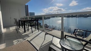 A balcony with a view of a body of water, a dining table, chairs, and a glass table. - Golden Bay 608, (Sunny Isles Beach)