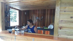 A wooden cabin interior with a kitchen area, including a counter, utensils, and a window.