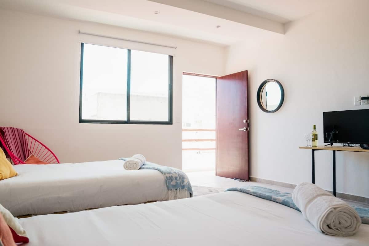 Una habitación de hotel con dos camas, un televisor, un espejo y una ventana.