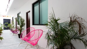A modern building with a concrete pathway, potted plants, and a pink chair. - Great Villas Studios & Residences - The Kahlo (Playa del Carmen)