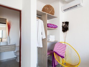 A bathroom with a wooden vanity, a mirror, a white towel, a woven basket, a purple pillow, and a yellow chair. - Great Villas Studios & Residences - The Kahlo (Playa del Carmen)