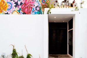 A modern building with a vibrant mural on the exterior wall, a dark entrance door, and a small balcony with plants. - Great Villas Studios & Residences - The Kahlo (Playa del Carmen)