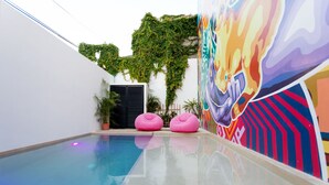 An indoor swimming pool with a mural, two pink bean bags, and a door with a black shutter. - Great Villas Studios & Residences - The Kahlo (Playa del Carmen)