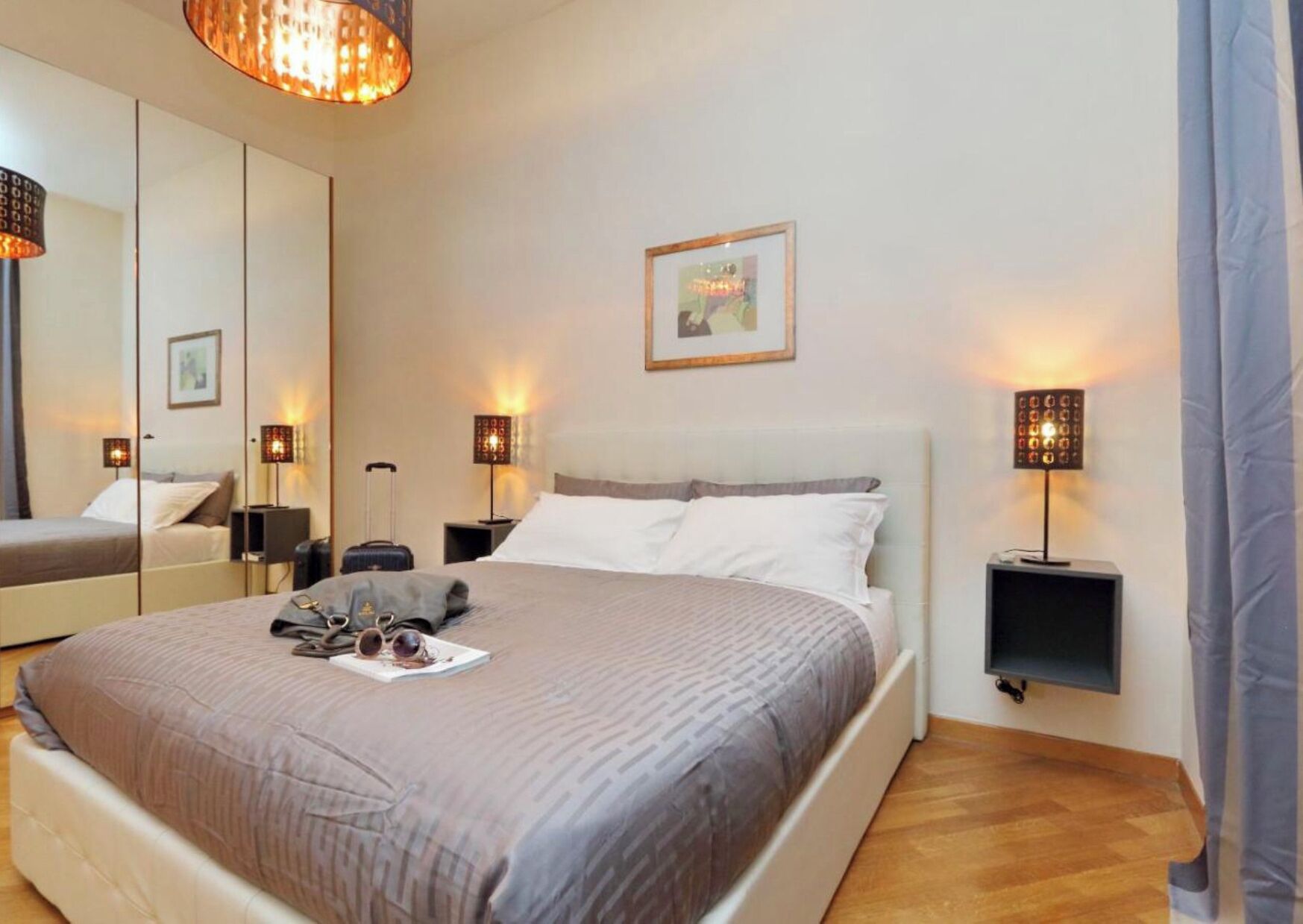 Quarto de hotel com cama grande, abajures, um espelho e um quadro na parede.