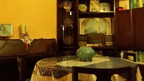 A dining area with a round table covered by a lace tablecloth, surrounded by wooden chairs. A green vase is placed on the table. - Myosotis (Introdacqua)