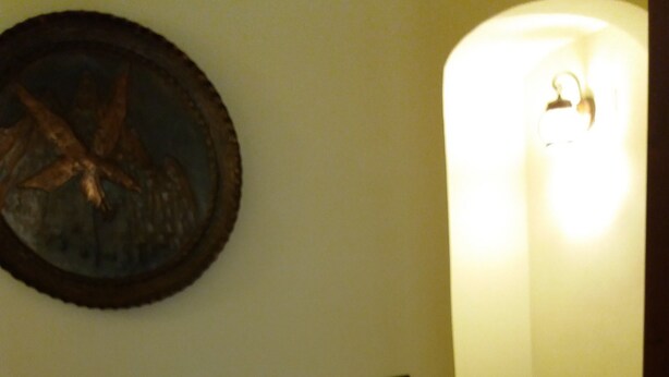 A hallway with a tiled floor, a wall-mounted light fixture, and a framed picture. - Myosotis (Introdacqua)