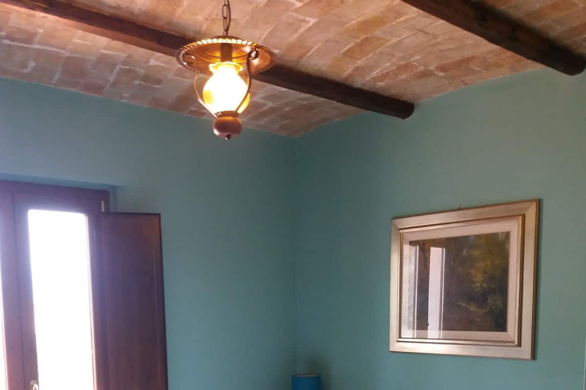 Une chambre à coucher avec un lit, une fenêtre, un tableau au mur et un luminaire suspendu.