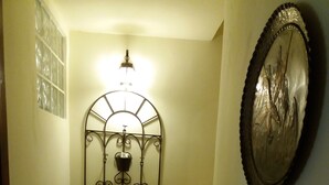 A narrow staircase with a metal wall-mounted light fixture and three potted plants. - Myosotis (Introdacqua)