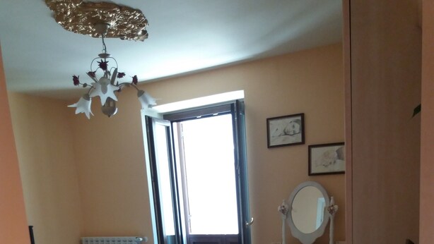 A bedroom with a bed, a desk with a mirror, and a radiator. - Myosotis (Introdacqua)