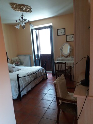 A bedroom with a bed, a desk with a mirror, and a radiator. - Myosotis (Introdacqua)