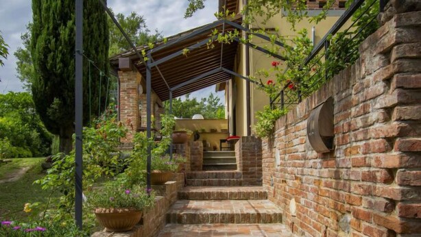 A brick staircase leading to a covered outdoor area with a pergola, surrounded by lush greenery and potted plants. - Aurelia by Interhome (Castelfiorentino)