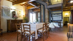 A dining area with a high ceiling, exposed wooden beams, and a brick wall. There is a table set for four with chairs, a clock, and a map on the wall. - Aurelia by Interhome (Castelfiorentino)