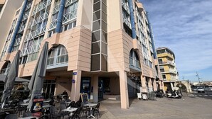 A multi-story hotel with a beige facade, large windows, and a ground-level bar area with outdoor seating.