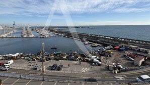 A marina with boats docked, a pier extending into the water, and a parking area with vehicles.