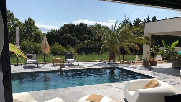 Un espace piscine extérieur moderne, doté de chaises longues et d’un petit coin salon.