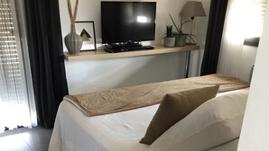 Une chambre d’hôtel avec un lit, un téléviseur posé sur un meuble, une lampe et une fenêtre avec des rideaux.