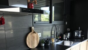 Une cuisine moderne avec un plan de travail noir, des armoires en bois, un évier en acier inoxydable et une fenêtre située au-dessus de l’évier.