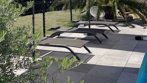 Un espace aménagé au bord de la piscine, comprenant deux parasols, des chaises longues et une piscine.