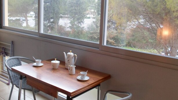 A room with a wooden table set for tea, a window with a view of trees and a parking lot. - 45m² Apartment in Balaruc-les-Bains, pets allowed (Balaruc-les-Bains)