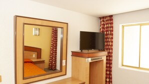 Una camera d'albergo con un letto, una televisione su un mobile in legno, uno specchio e una finestra con tende.