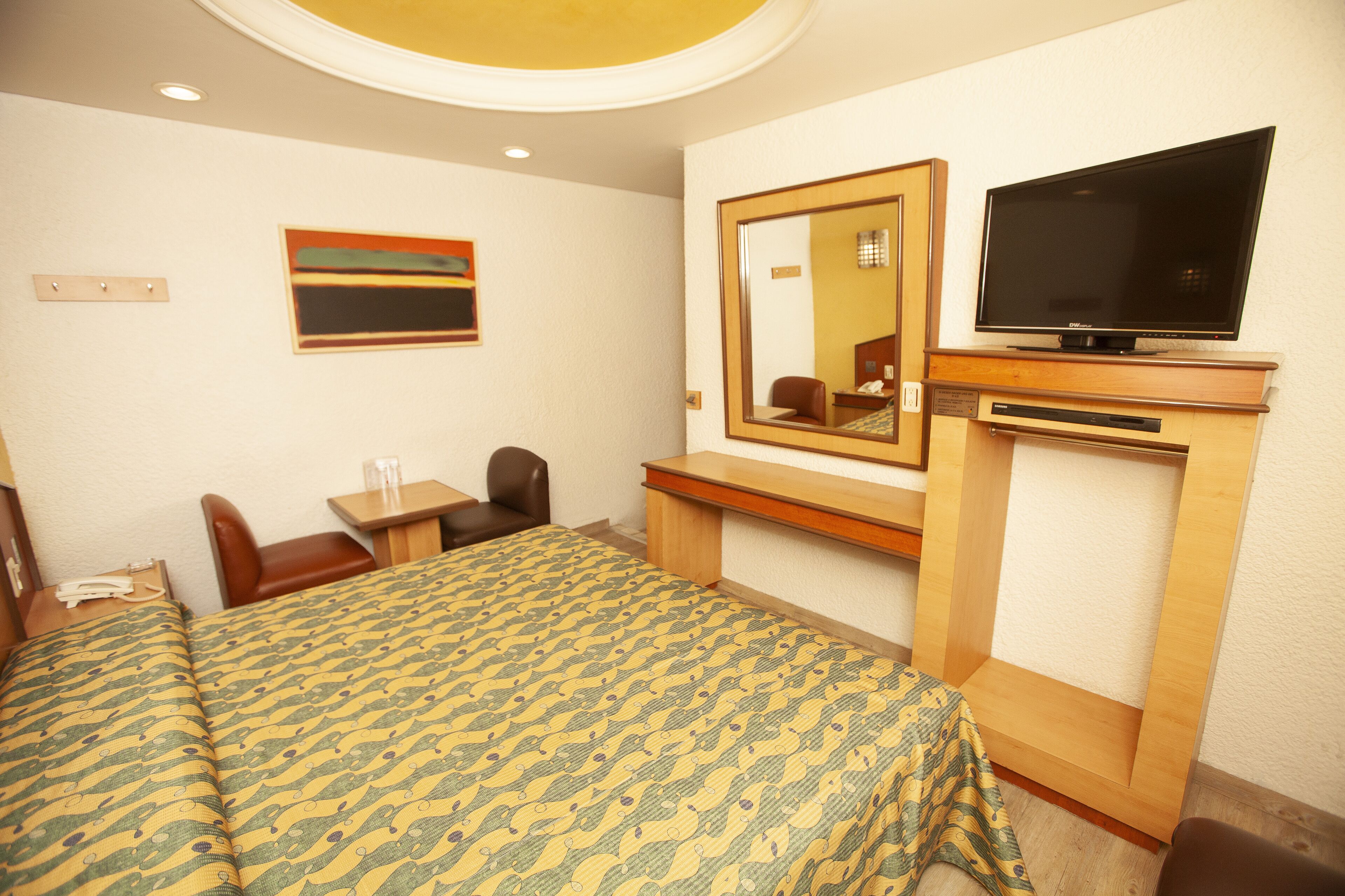 A hotel room with a bed, a desk, a chair, a television, and a mirror.