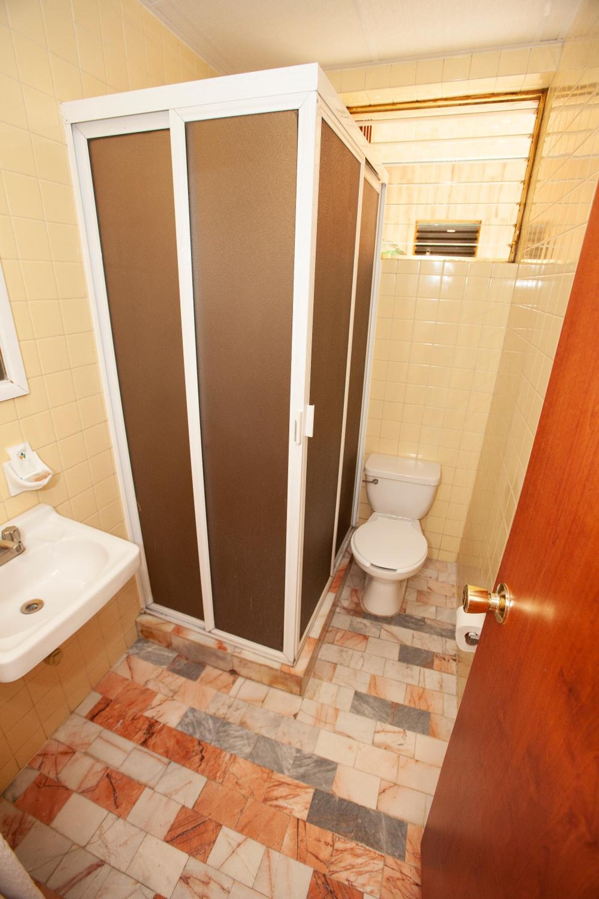 A bathroom with a shower enclosure, toilet, sink, and tiled floor.