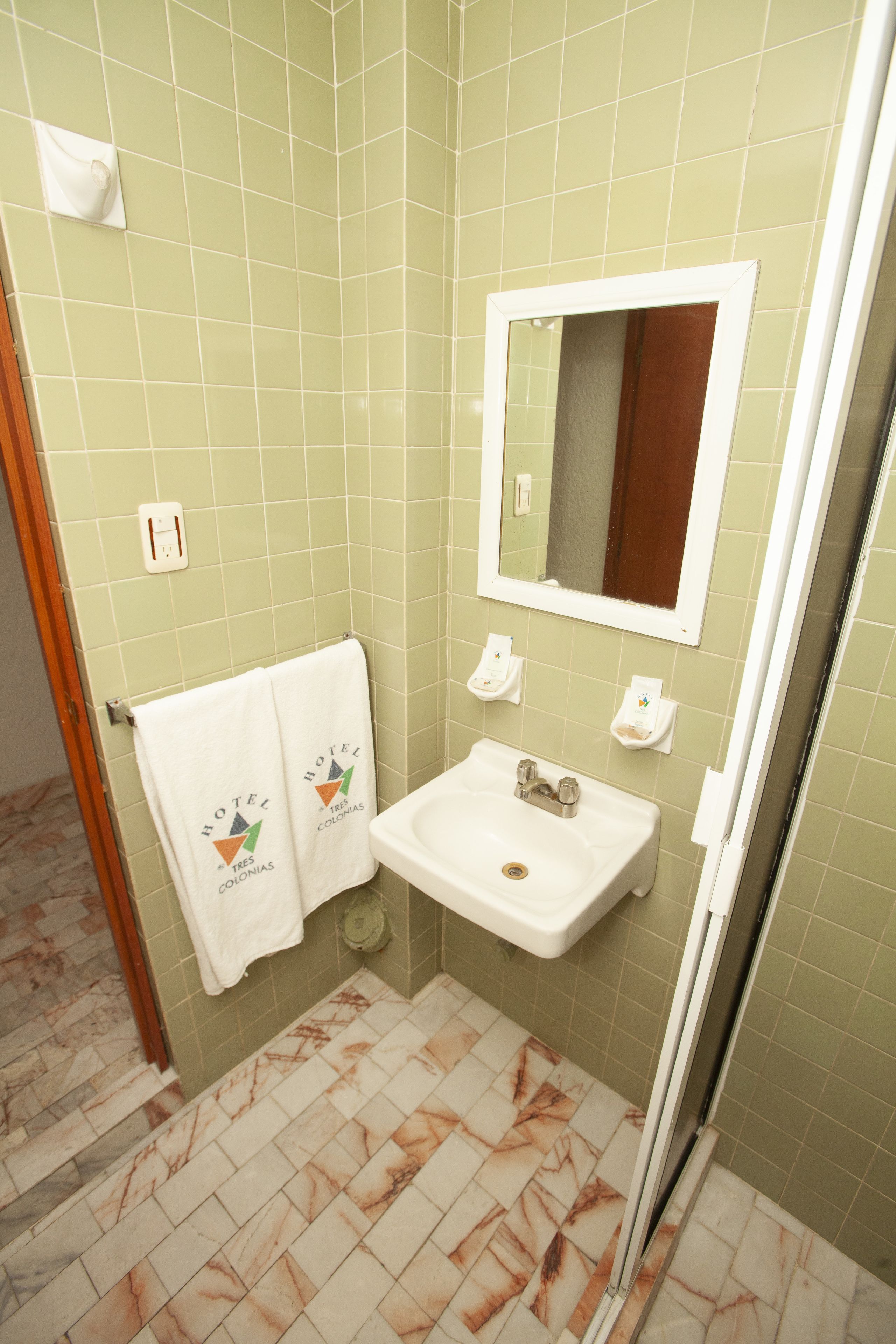 A bathroom with a sink, mirror, and green tiled walls.