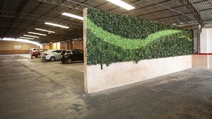 Un parcheggio con una parete verticale ricoperta da un giardino verde e diverse auto parcheggiate.
