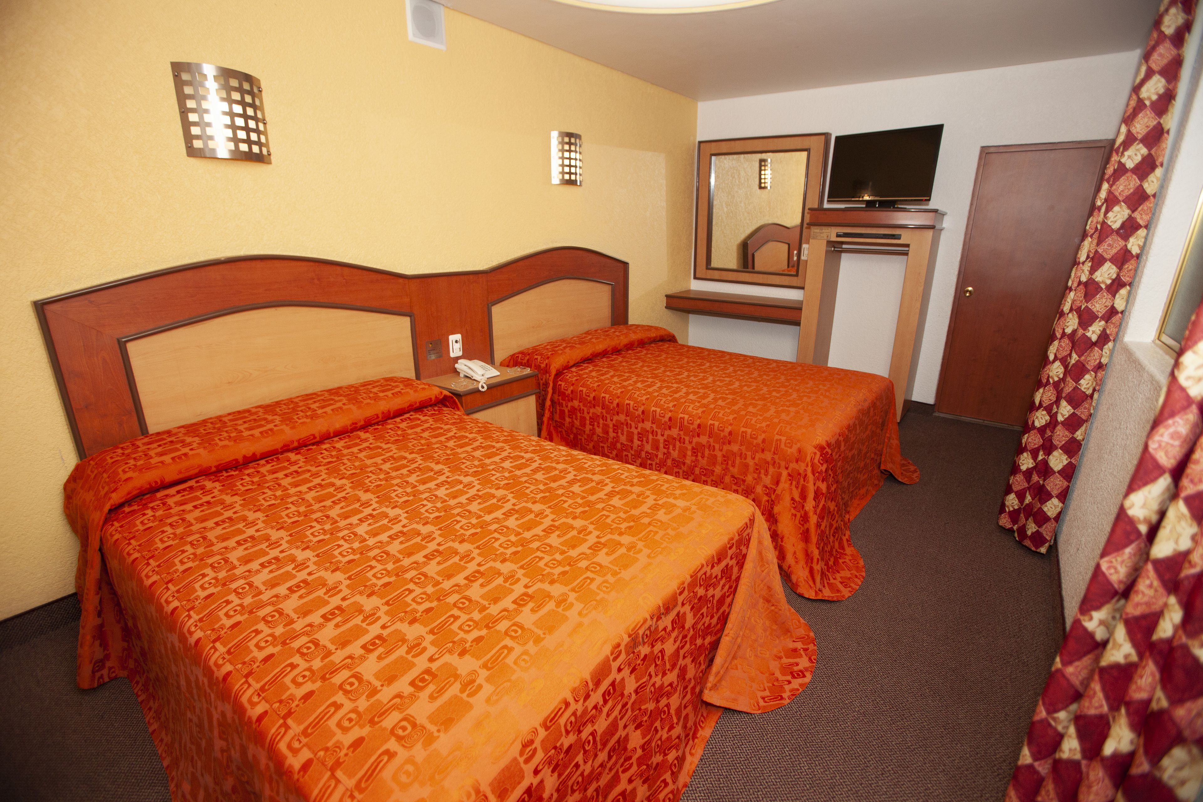 Una habitación de hotel con dos camas, televisión y espejo.