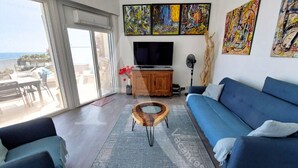 A living room with a sofa, a coffee table, a TV, and artwork on the wall. - APPARTEMENT 3 CHAMBRES, GARAGE, LARGE TERRASSE VUE UNIQUE (Sète)