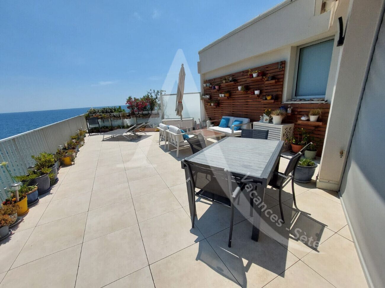 A rooftop terrace with a table and chairs, potted plants, and a view of the sea.