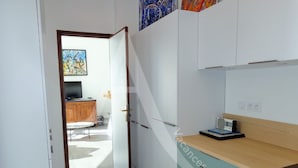 A modern kitchen with white cabinets, a wooden countertop, and a built-in oven. There is a dining area visible in the background with a wooden table and chairs. - APPARTEMENT 3 CHAMBRES, GARAGE, LARGE TERRASSE VUE UNIQUE (Sète)