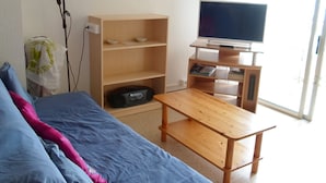 Una habitación con una cama, una mesita de madera, un televisor en un mueble bajo y una estantería.