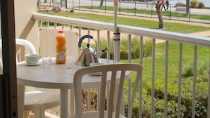 Un balcón con una mesa preparada para dos personas, una tetera, una botella de jugo y una taza.