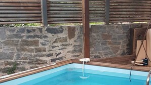 Et rektangulært pool med træterrasse og baggrund af stenvæg.