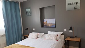 Et soveværelse med en seng, to sengeborde, en lampe, et billede på væggen og et gardin.