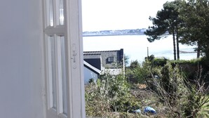 A view through a window with a white frame, overlooking a body of water, trees, and buildings. - "Secrets of Petit Rohu" - 2ch, garden & beach (Saint-Pierre-Quiberon)