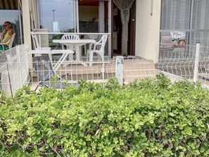 Un espace extérieur clos, avec une table et des chaises, un coin salon abrité et une haie au premier plan.