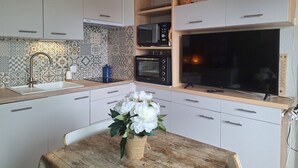 A modern kitchen with white cabinets, a wooden countertop, a built-in microwave, oven, and a large TV. There is a vase with flowers on the table.