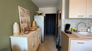 A compact kitchen with a refrigerator, a sink, and a microwave. There is a dining table with chairs and a small cabinet.
