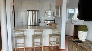 A modern kitchen with white cabinetry, stainless steel appliances, and a central island with bar stools. - OCEANFRONT Villa in Mariners Watch! (Kiawah Island)