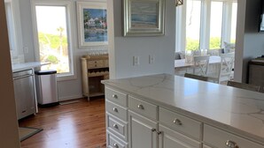 A modern kitchen with white cabinetry, a marble countertop, and a view of the outdoors through large windows. - OCEANFRONT Villa in Mariners Watch! (Kiawah Island)