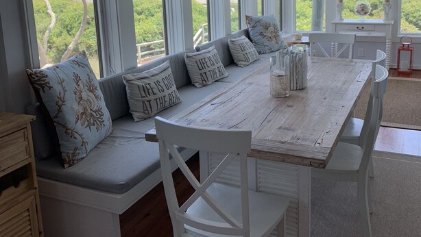 A spacious room with a large window overlooking a scenic view, a wooden dining table, and a built-in bench with cushions. - OCEANFRONT Villa in Mariners Watch! (Kiawah Island)