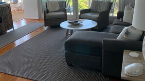 A modern living room with a sofa, two armchairs, a coffee table, and a TV. There are large sliding glass doors leading to a balcony with a view of the ocean. - OCEANFRONT Villa in Mariners Watch! (Kiawah Island)
