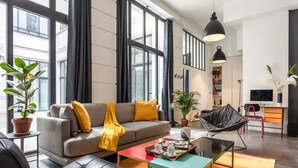 Un salon moderne avec un canapé gris, un plaid jaune, un fauteuil en cuir noir, une table basse et un meuble pour la télévision avec un écran plat.