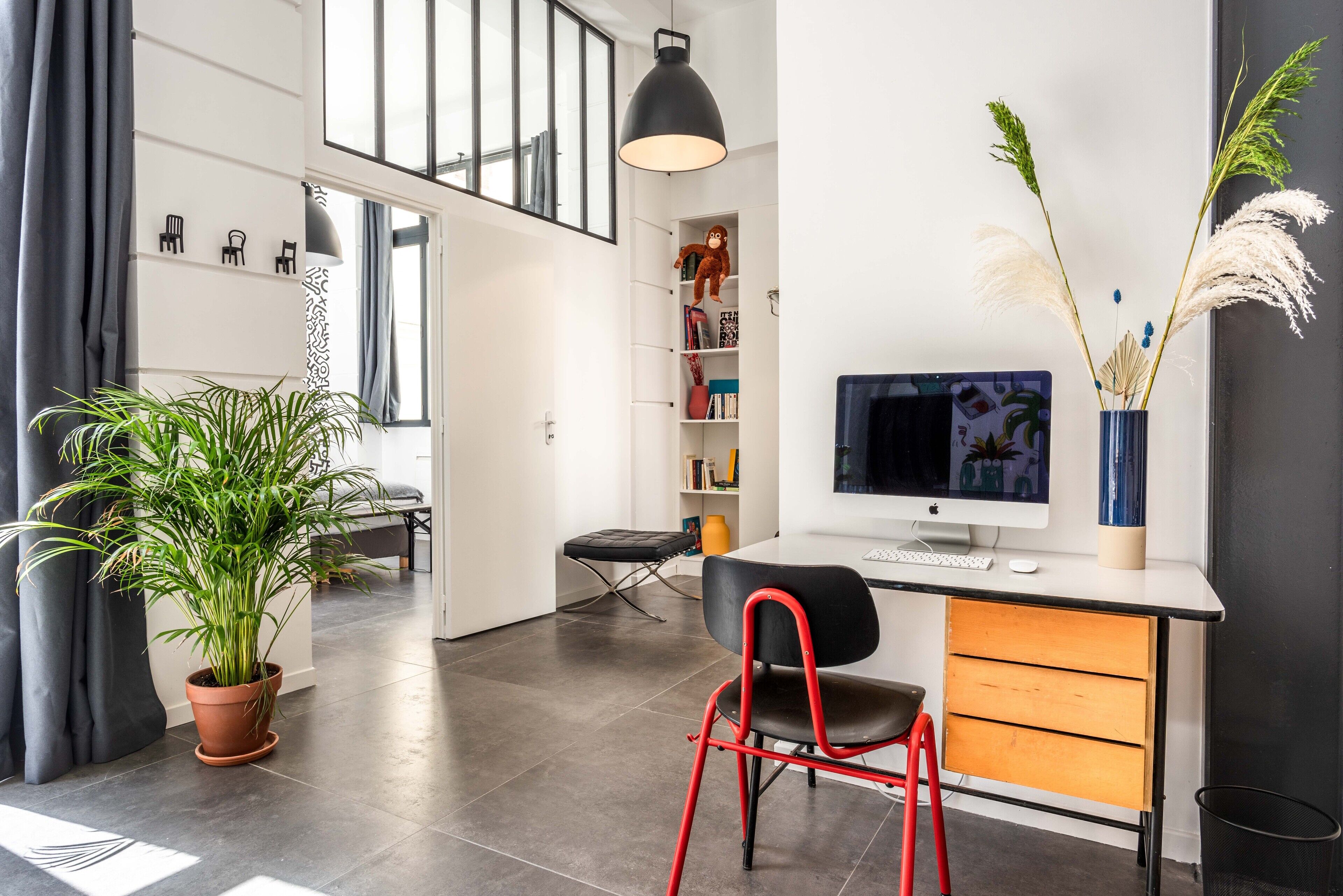 A modern office space with a desk, chair, and computer. There is a potted plant and a shelf with decorative items.