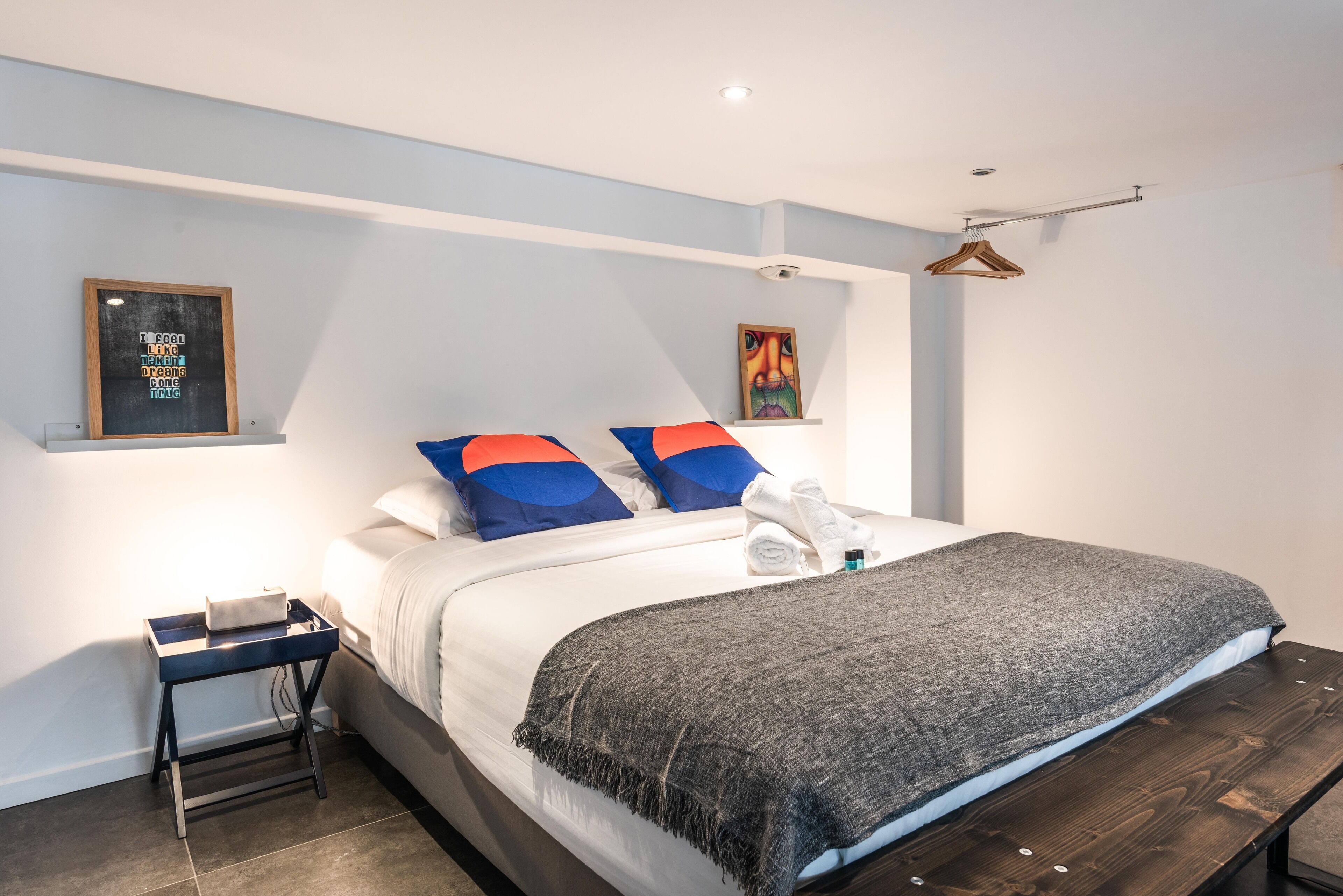 Un dormitorio moderno con cama, mesita de noche y una repisa con obras de arte.